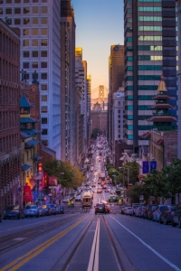 Photo of the San Francisco, California downtown downhill at dusk, showing the San Francisco Bay Bridge in the far background.